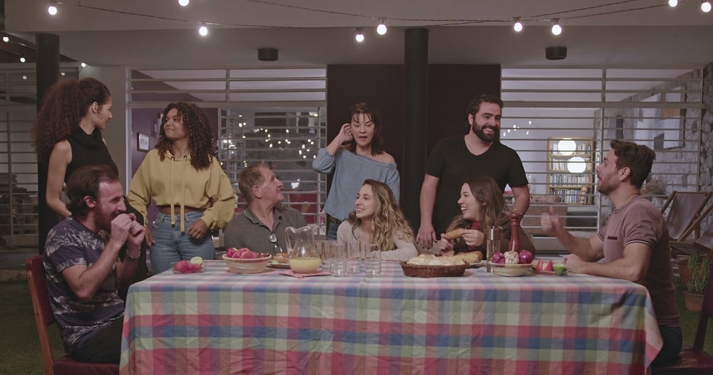 A group of diverse friends and family members of various ages laughing and talking around a large dinner table