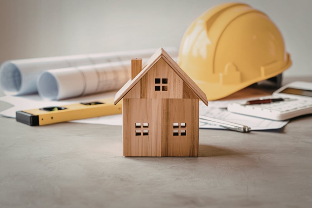 An eye-level, close-up shot of a small wooden house model in the foreground