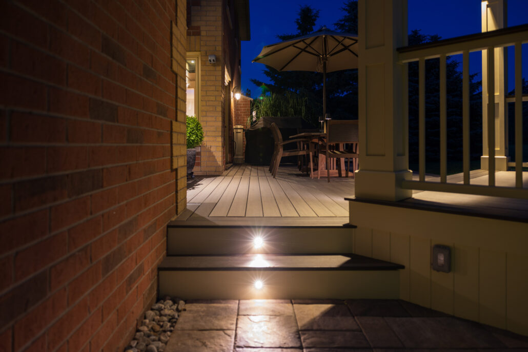 Illuminated outdoor timber deck with step lights and alfresco dining area at night beside a brick home in Lake Macquarie