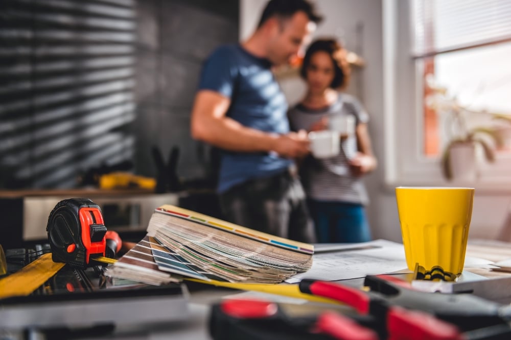 A close-up of home renovation tools, color swatches, and a yellow mug on a table