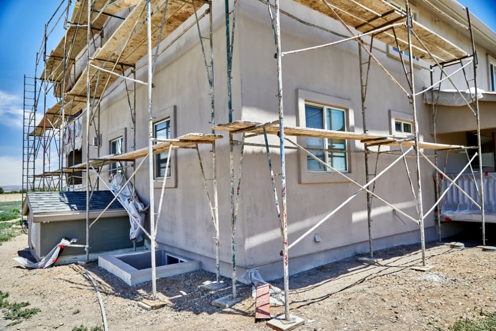 A tan two-storey house surrounded by metal scaffolding with wooden planks, indicating ongoing exterior construction