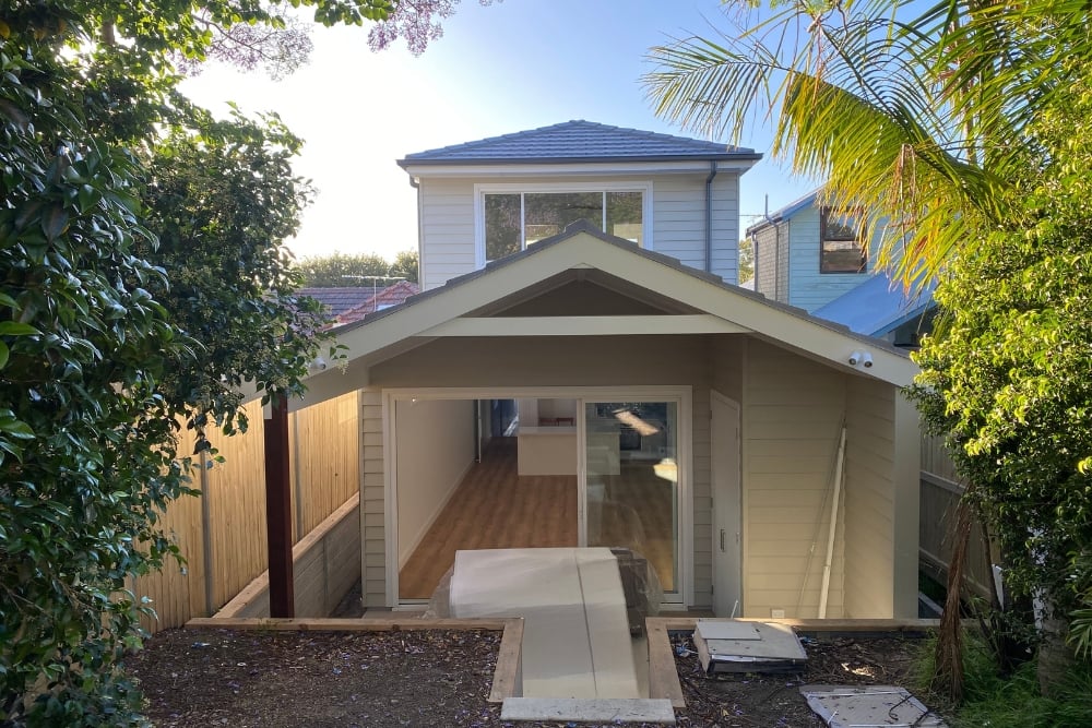 A view from a backyard looking toward a modern two-storey home extension with a gabled roof and large sliding glass doors.