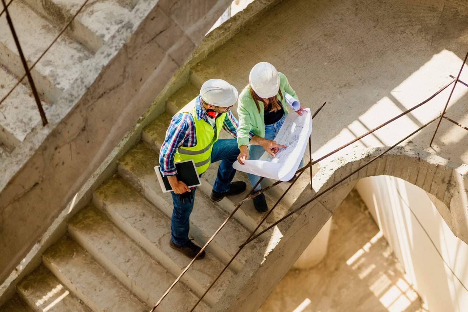 Woman architect explaining building plans to construction supervisor on concrete staircase at active building site in Beresfield Newcastle