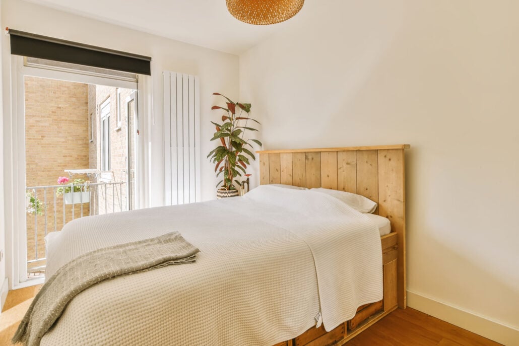 Bright bedroom extension with timber bed frame, indoor plant and balcony access showing natural light and open layout in Beresfield home extension