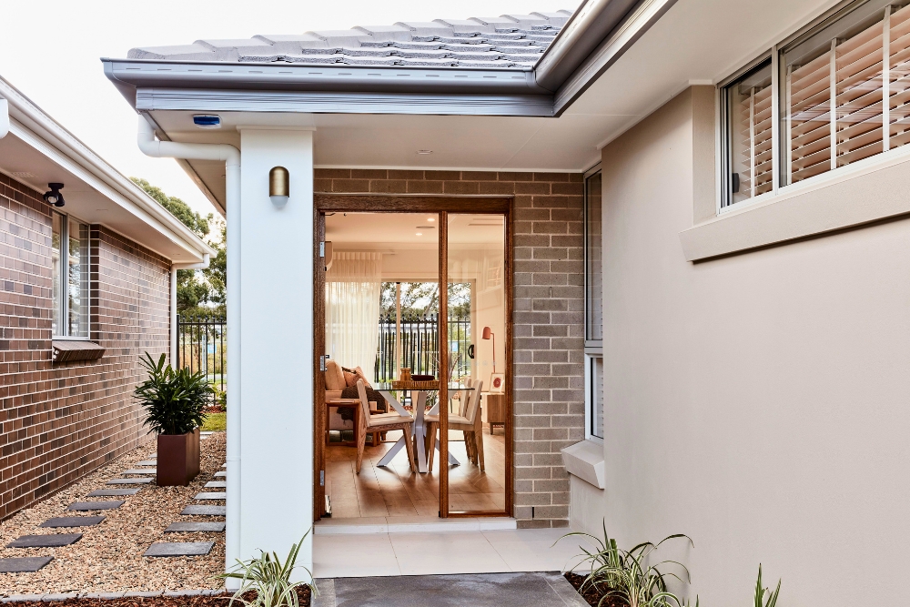 An exterior view of a modern brick home with a glass sliding door that reveals a warmly lit dining room and living space inside.