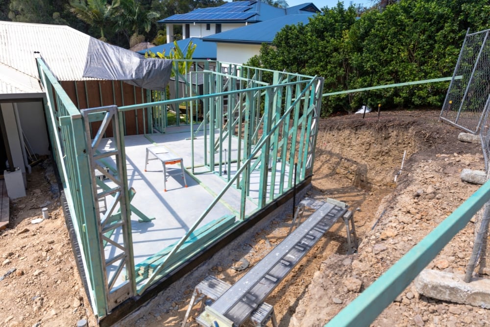 A green timber house extension frame erected on a concrete slab at a residential construction site