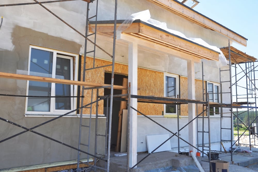A residential building extension under construction surrounded by metal scaffolding.