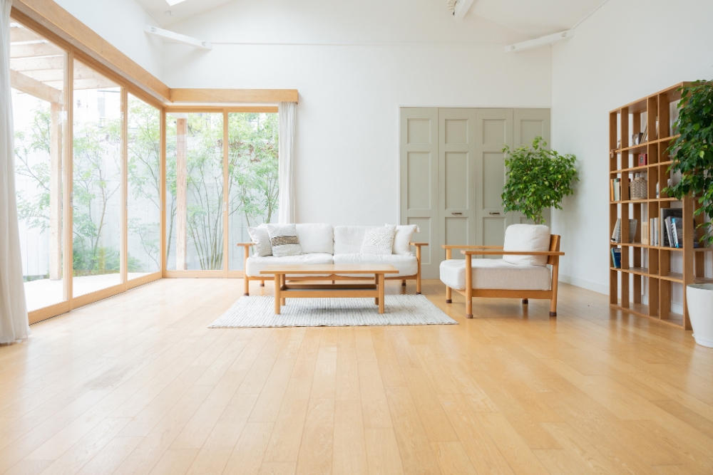 A bright, sunlit modern living room with light hardwood floors, featuring a white sofa and armchair with wooden frames
