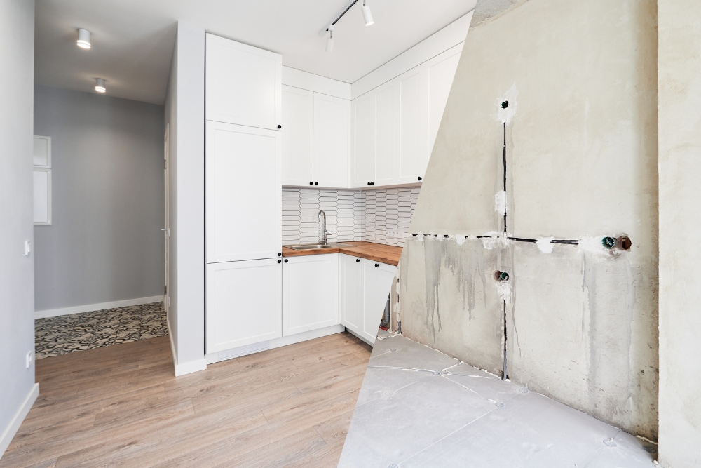 A split image showing a kitchen renovation, with an unfinished concrete construction wall on the right and the completed modern white kitchen on the left.