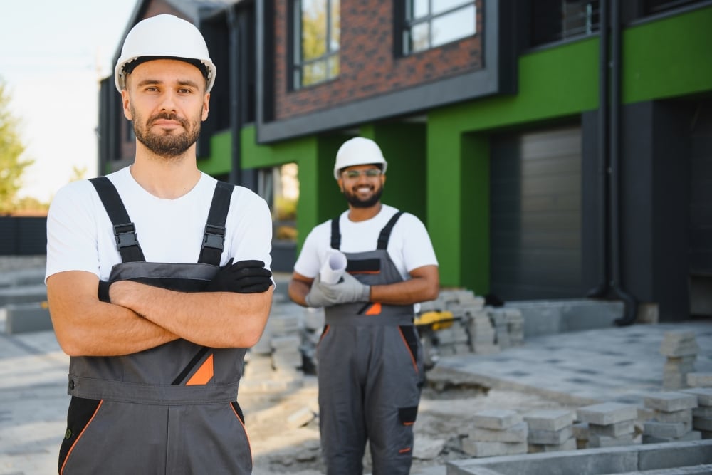 Two construction workers wearing hard hats standing in front of a modern residential building site.