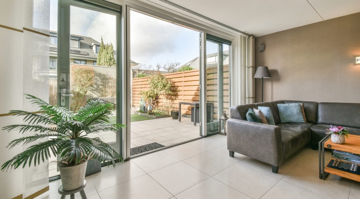 A wide shot of a modern living room featuring a large grey sectional sofa and tile flooring