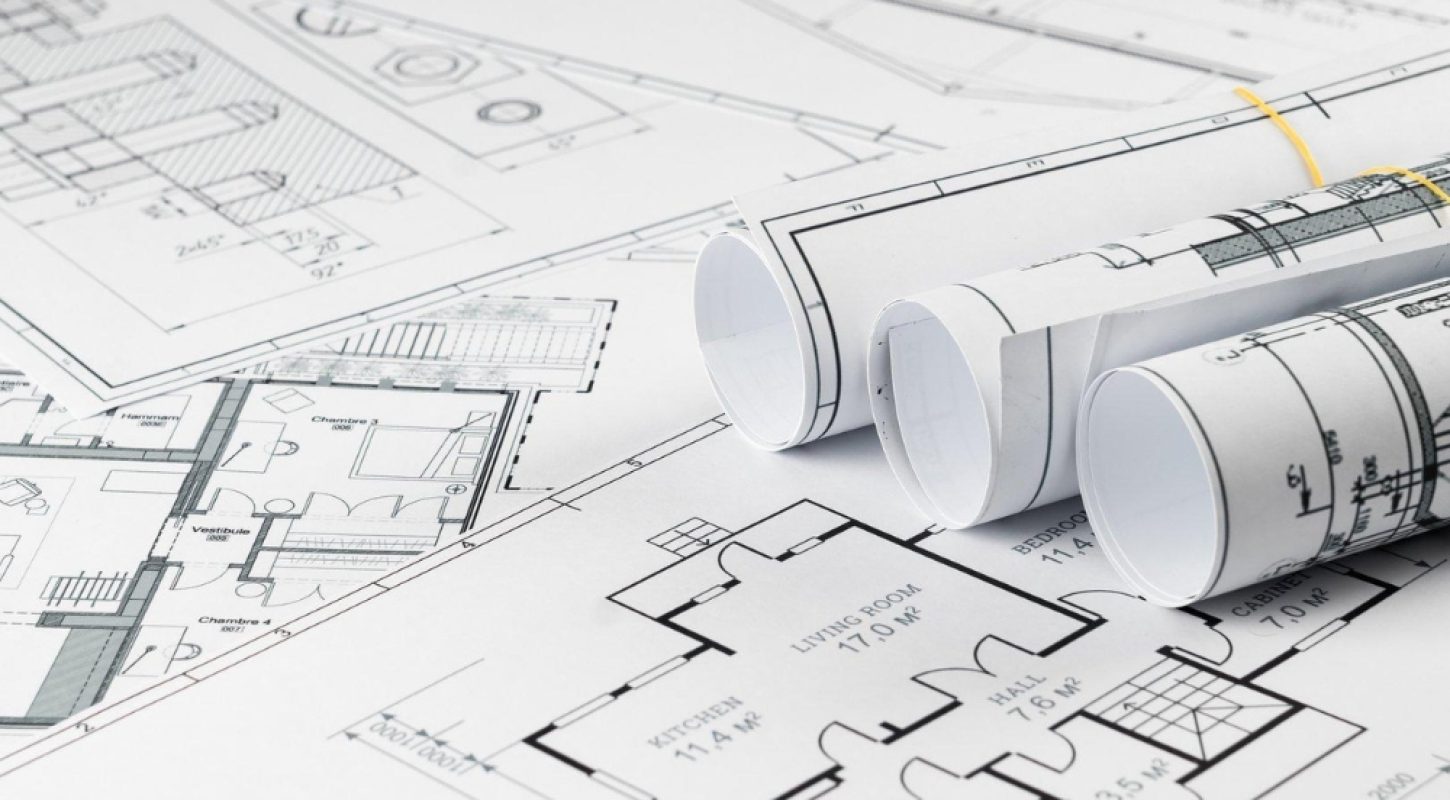 Three rolled-up architectural blueprints resting on a flat, detailed floor plan layout with visible room dimensions and labels.